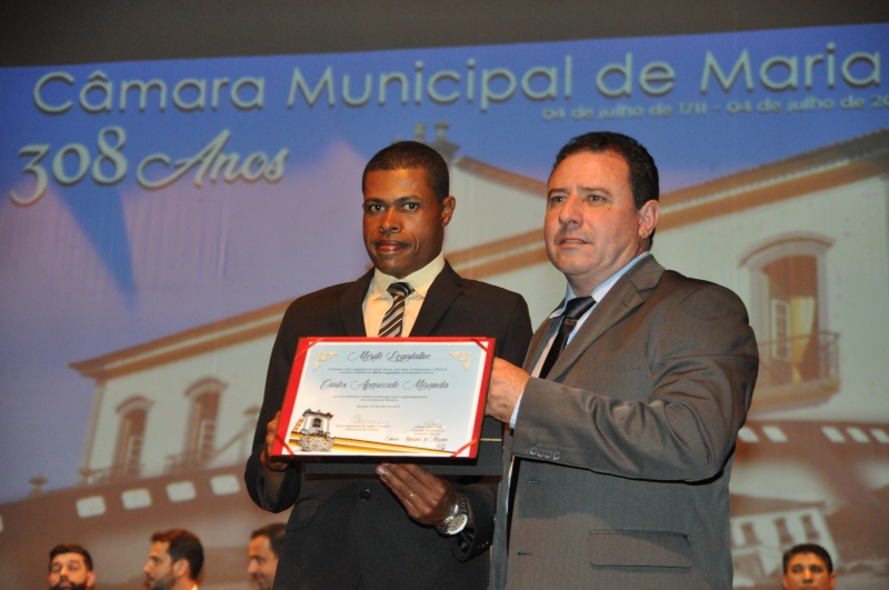 Carlos Miranda recebe o Mérito Legislativo pelas mãos do vereador Adimar José Cota (PSC).